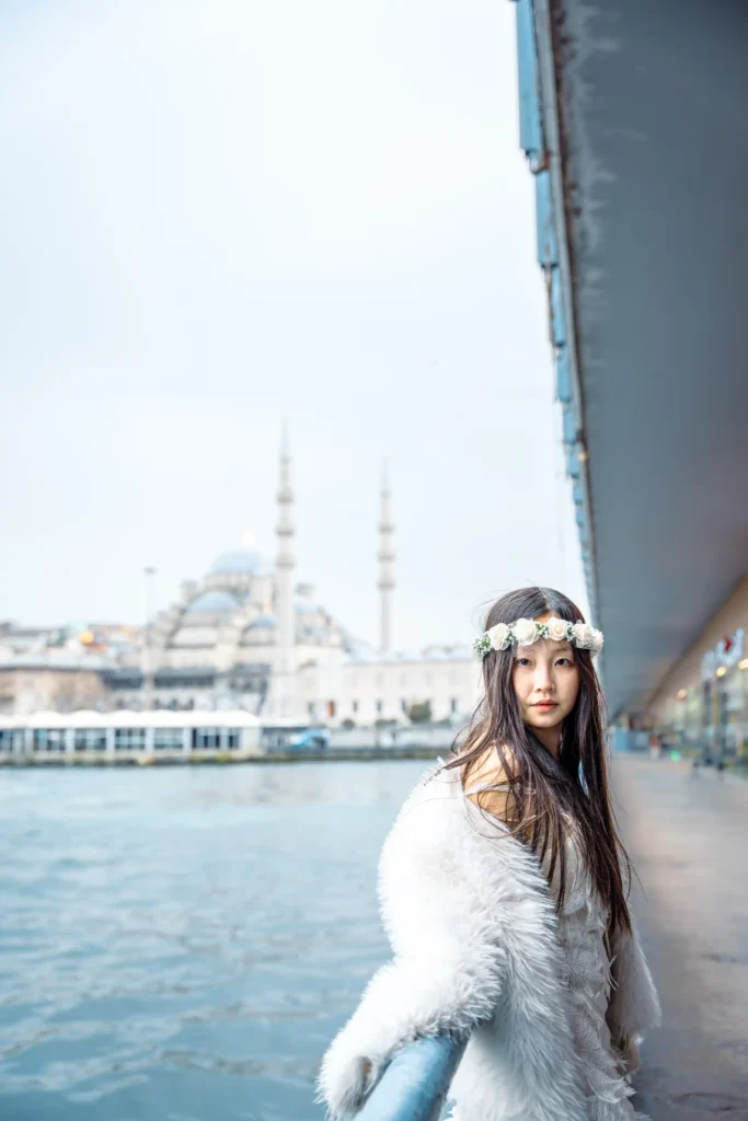 Embarking on a photo shoot at the iconic Galata Bridge in Istanbul, featuring the stunning backdrop of the New Mosque, with a Singaporean girl promises to capture a mesmerizing blend of cultures, history, and natural beauty. As the Singaporean girl stands against the backdrop of the majestic New Mosque, with the Galata Bridge stretching gracefully across the Golden Horn below, the scene becomes a timeless tableau of contrasts and harmonies.